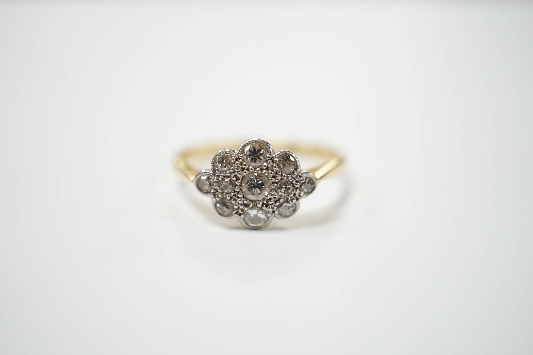 A 1920's 18ct, plat and millegrain set diamond cluster ring, size P, gross weight 3 grams.
